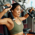 Asian female athlete doing weight exercises for upper body strength during sports training in a gym.