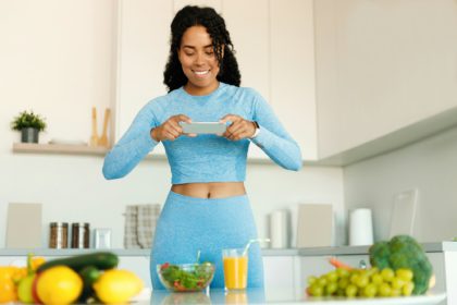 Food and fitness blogging concept. Fit black lady taking photo of healthy dinner on smartphone