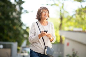 happy older woman laughing with mobile phone outside
