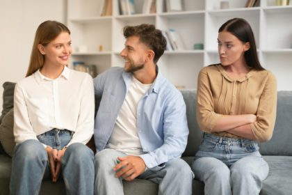 man hugs girlfriend while another woman looks with jealousy indoor