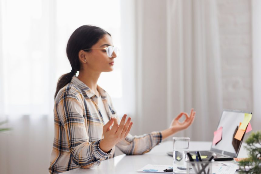 Managing stress in the workplace. Hindu student girl meditating and relaxing during a busy day while