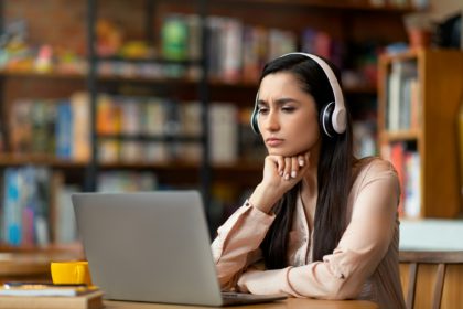 Online education concept. Concentrated latin woman studying online at cafe, using laptop and headset